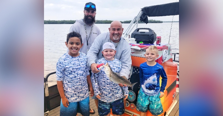 two men, including william "big will" dunn, posing with three young boys on a boat with a fish they caught for the organization take a kid fishing