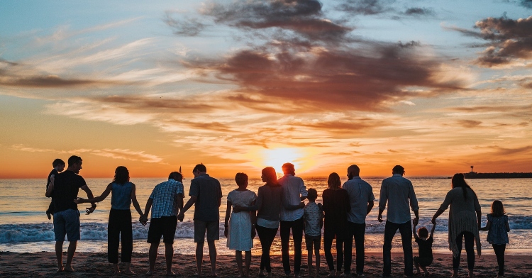 group of people standing on beach at sunset