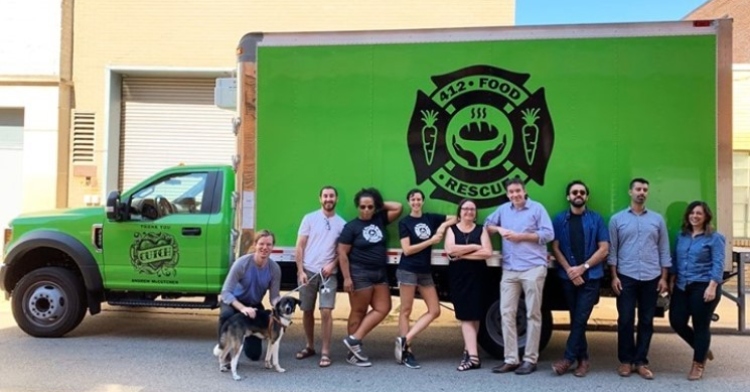several people and a dog posing in front of a large green truck with the 412 food rescue non-profit logo on the side