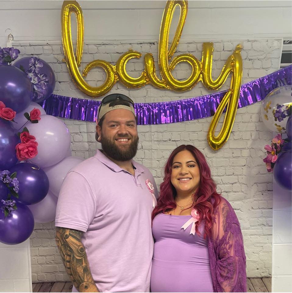 couple standing in front of balloons spelling baby