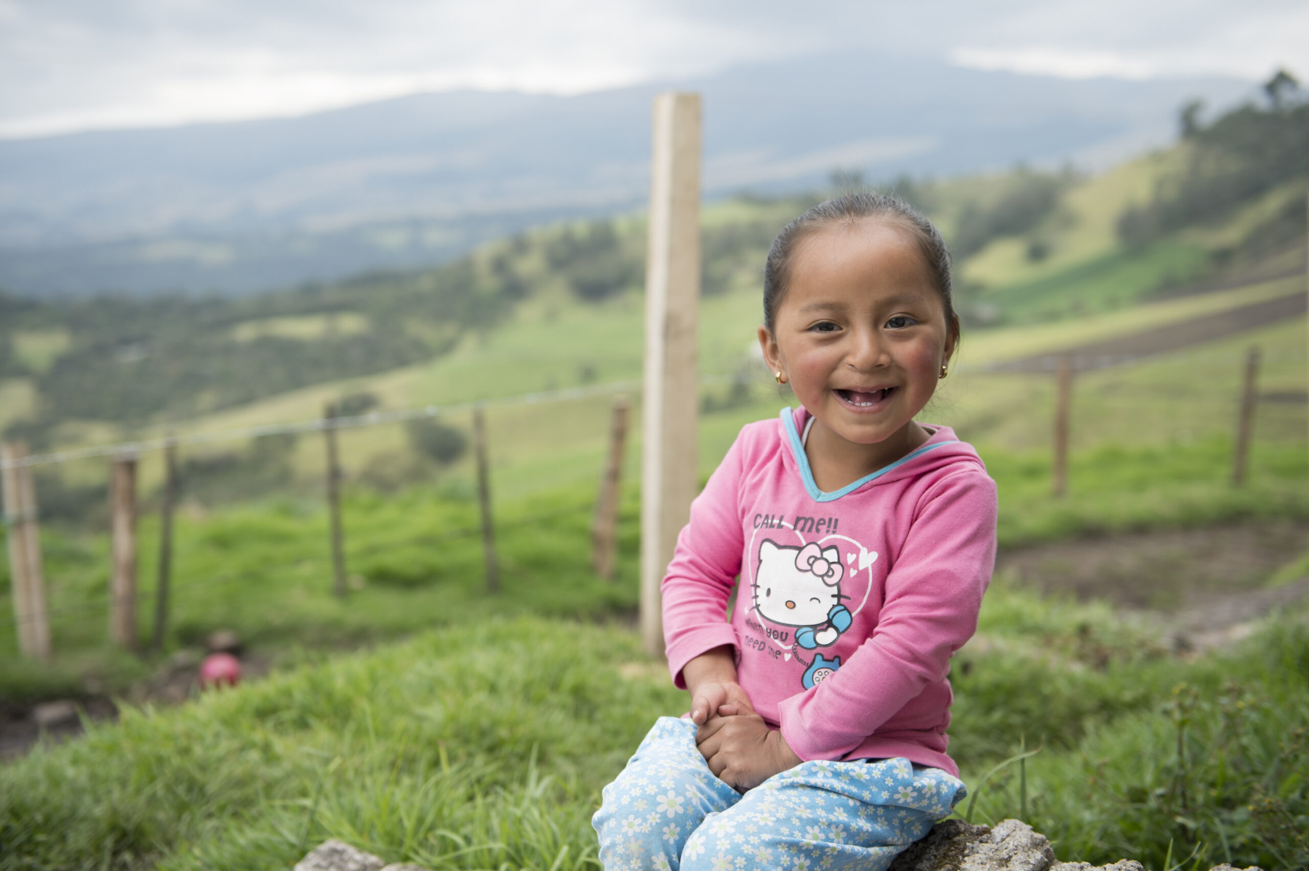 a little girl named fernanda cuchipe from ecuador sitting outside and smiling with mountains in the distance