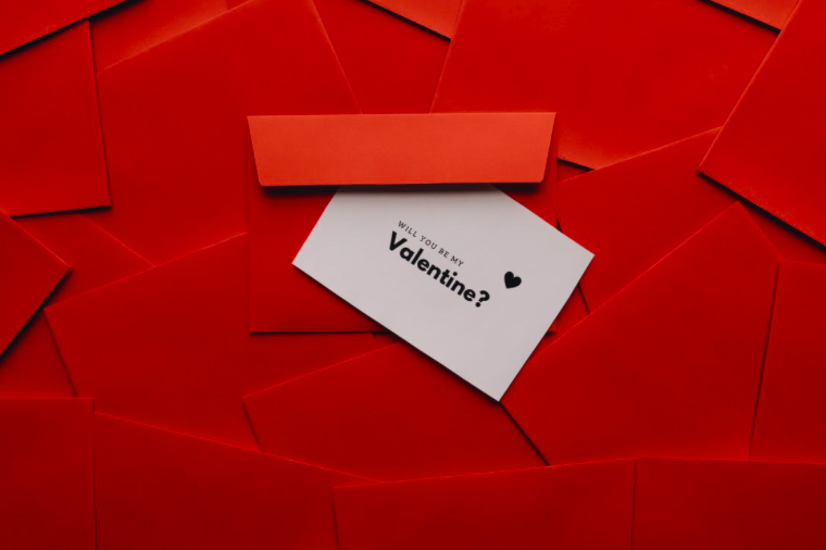 card on top of red envelopes that reads "will you be my valentine?"
