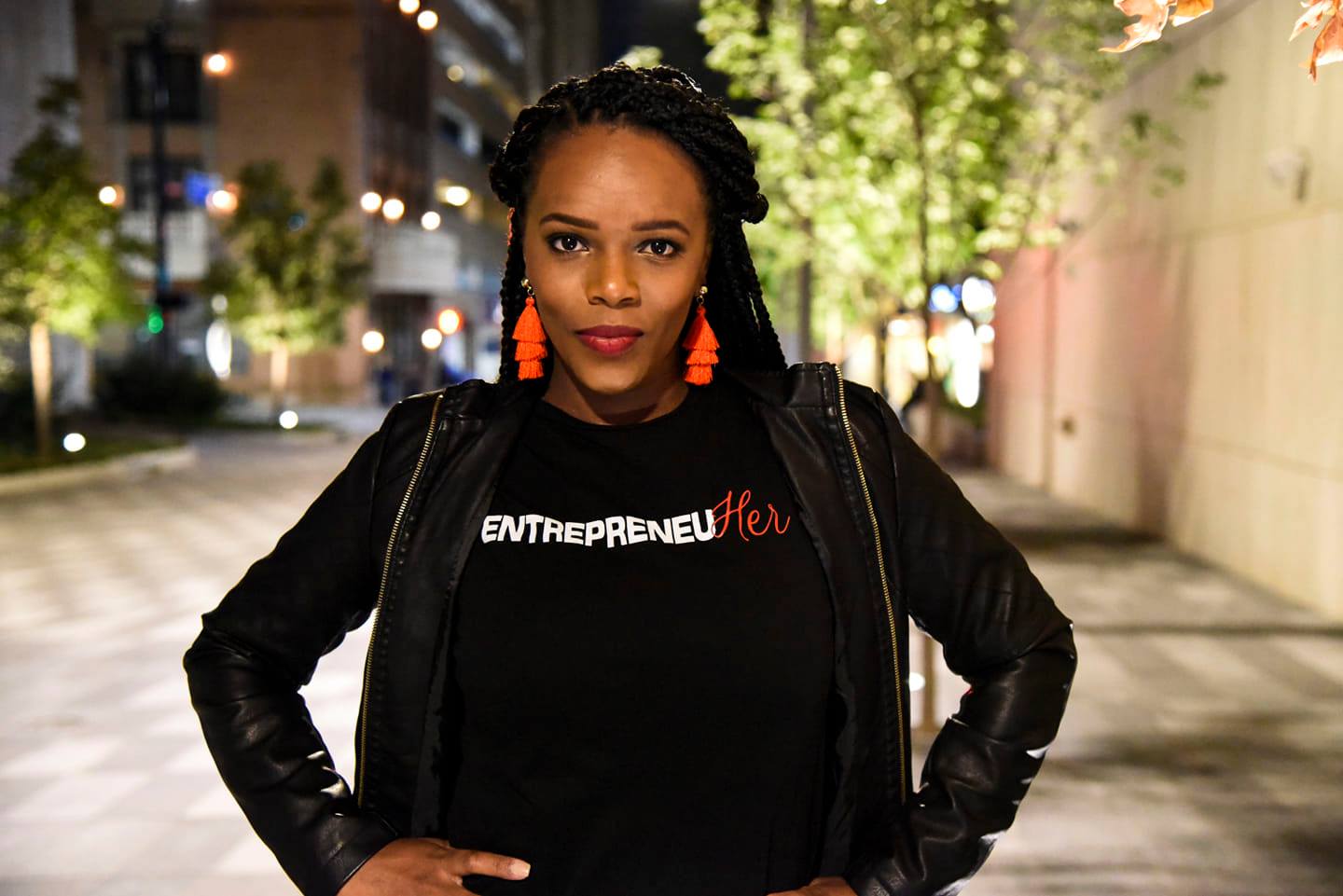 a woman named deidra mayberry posing outside with her hands on her hips as she wear a shirt that reads, "entrepreneuher"