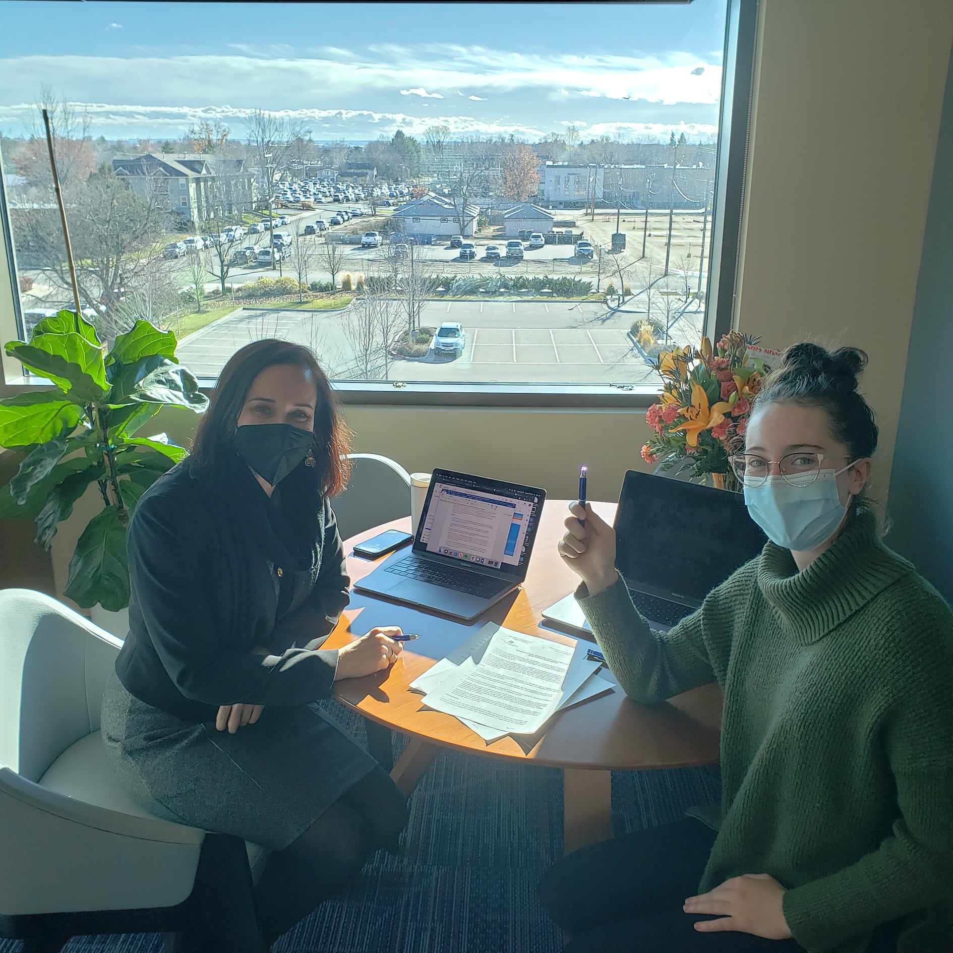 two women, one of them named ally orr, wearing face masks as they sit at a table reading over and signing documents next to their laptops at boise state university