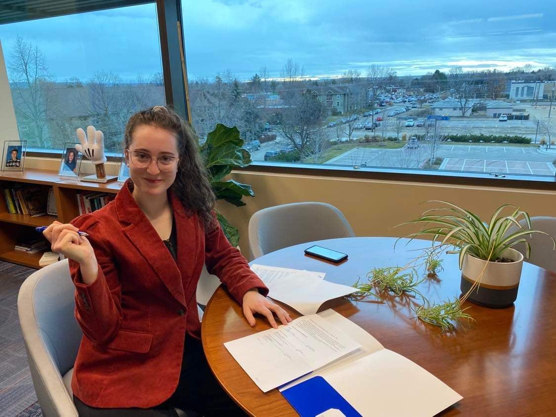 woman named ally orr smiling as she holds a pen in one hand while sitting at a table to sign papers for the women in stem, medicine, and law scholarship she's creating at boise state university