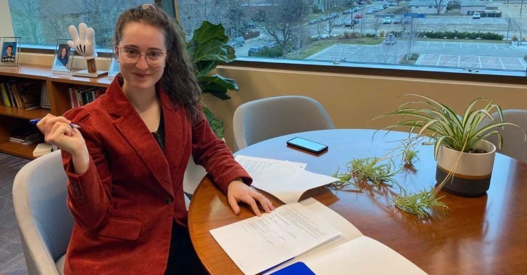 woman named ally orr smiling as she holds a pen in one hand while sitting at a table to sign papers for the women in stem, medicine, and law scholarship she's creating at boise state university