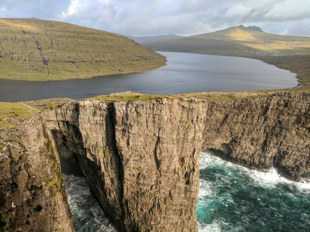 the Faroe Islands, with a lake at the top of a cliff and the ocean at the bottom