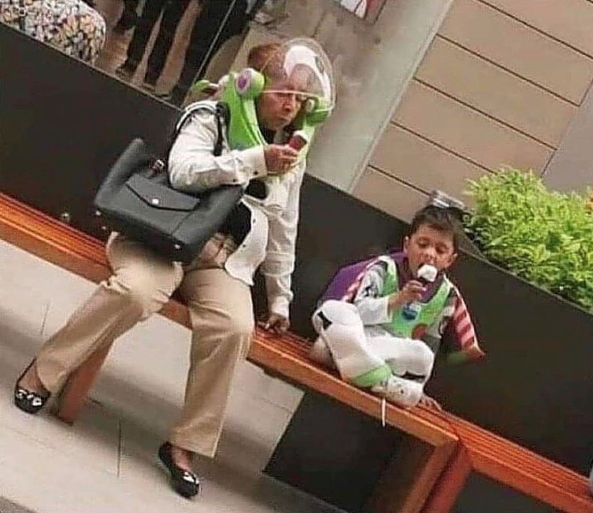 a grandma and her grandson each dressed like buzz lightyear from the animated film, toy story. while they sit on a bench and eat ice cream cones