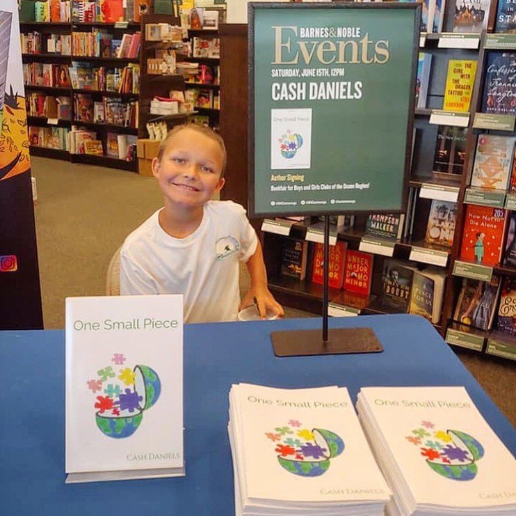 little boy named cash daniels smiling while sitting at a table at his barne's & noble book signing for his book 