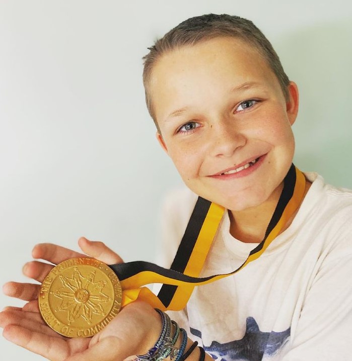 little boy named cash daniel smiling as he shows off the medal he's wearing around his neck