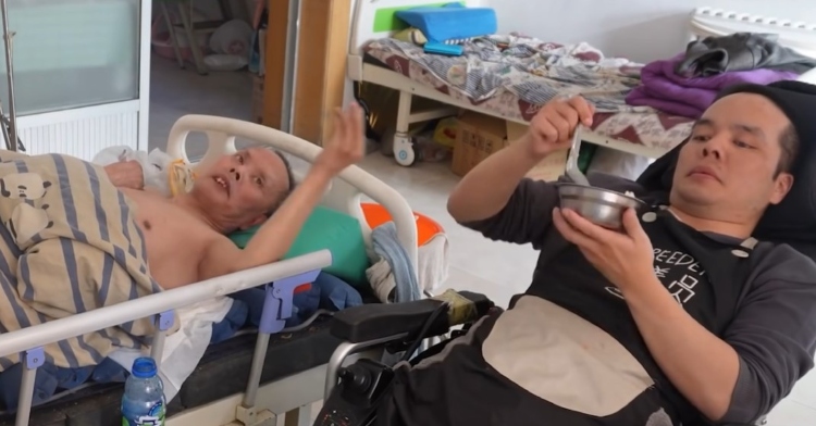 a disabled man in a wheelchair named zhang xiaodong who is helping to feed his dad who is paralyzed and laying in a bed next to him