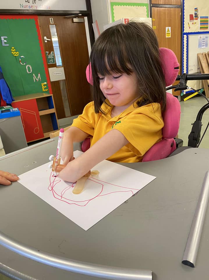 a 5 year old girl who has arthrogryposis multiplex congenita called ella who is siting in a chair and drawing