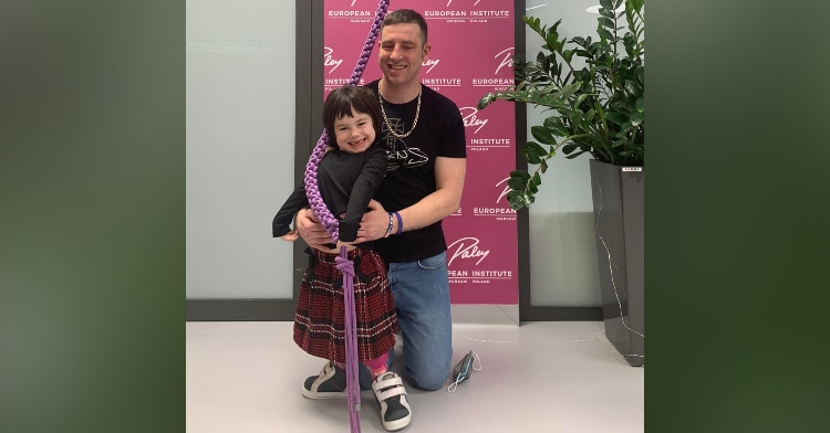 a 6 year old girl named ella green and her dad, william green, smiling as they pose with the bell at the european institute in poland