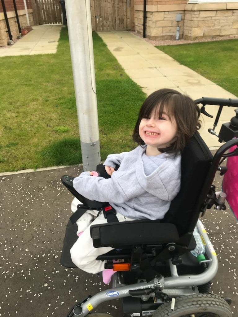 a 5 year old little girl called ella smiling while outside as she sits in her wheelchair