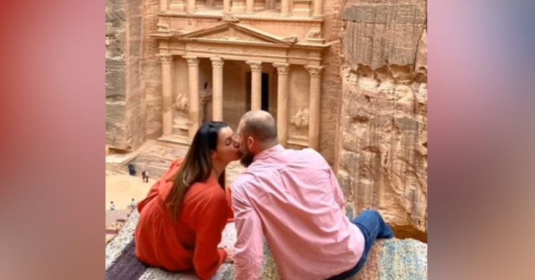 a woman named tatiana and a man kissing as they sit on a ledge with a scenic background