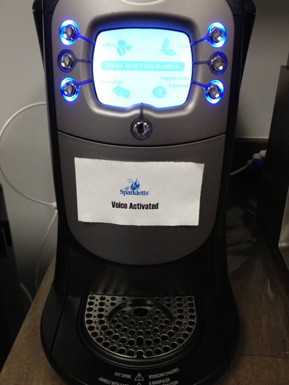office coffee maker with a sign taped on that says "voice activated"