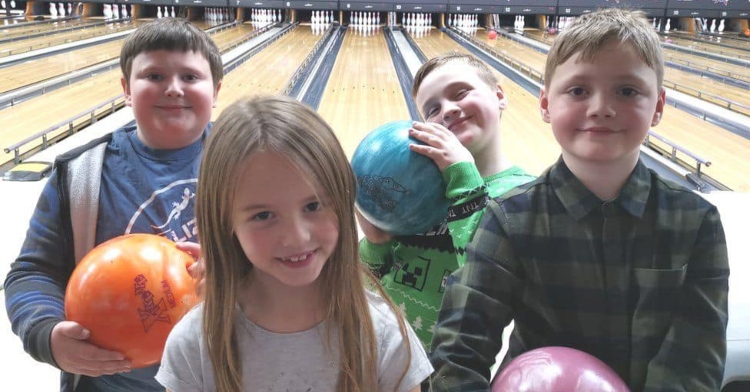 an 11 year old boy named harry brinkworth holding a bowling ball and smiling as he poses with three kids his age while in a bowling alley
