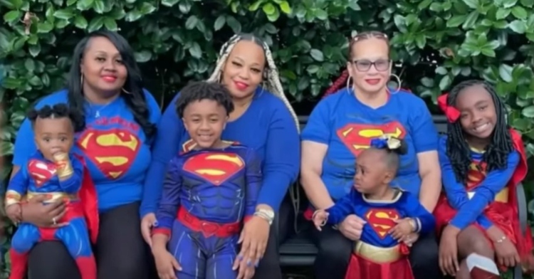 three women and four children, including 6-year-old kayden reid and 2-year-old kaylee reid, sitting on bench outside as they smile and pose in superman shirts or costumes