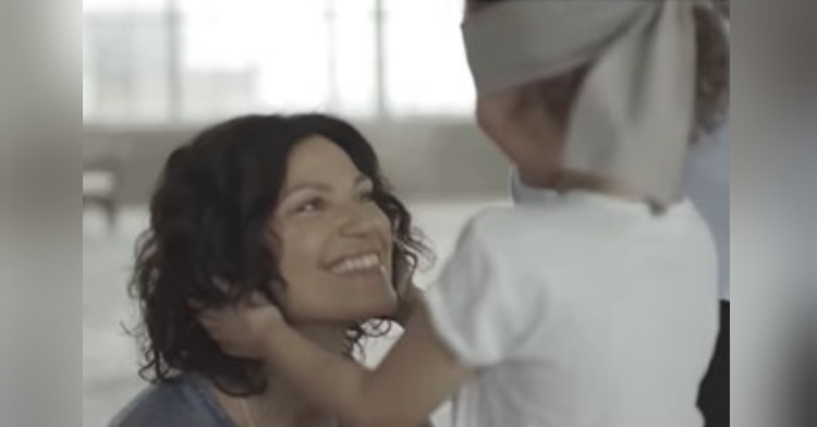 mom smiling up at her little girl who is blindfolded and touching her hair