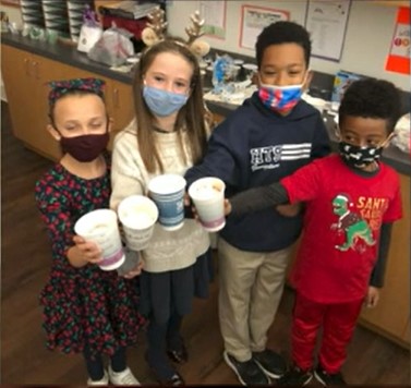 four third grade students posing with their hot chocolate cups as they wear face masks