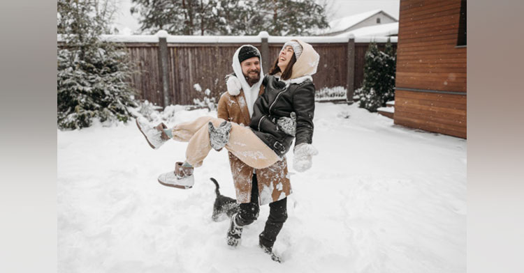 man carrying woman through snow while they laugh