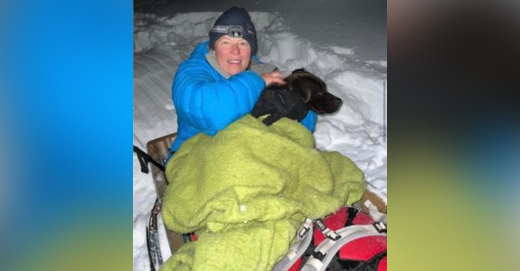 a woman named leona allen smiling as she snuggles with a black dog, russ, on a sled as they rescue him