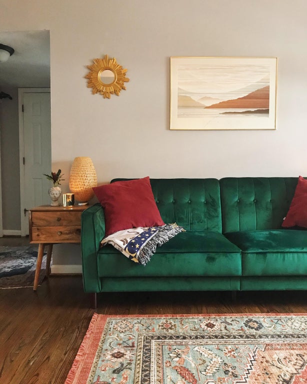 a well decorated living room with a green couch, rug, side table, and a painting