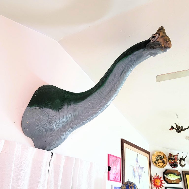 a large dinosaur wall dÃ©cor with a long neck hanging above a curtain on someone's wall  