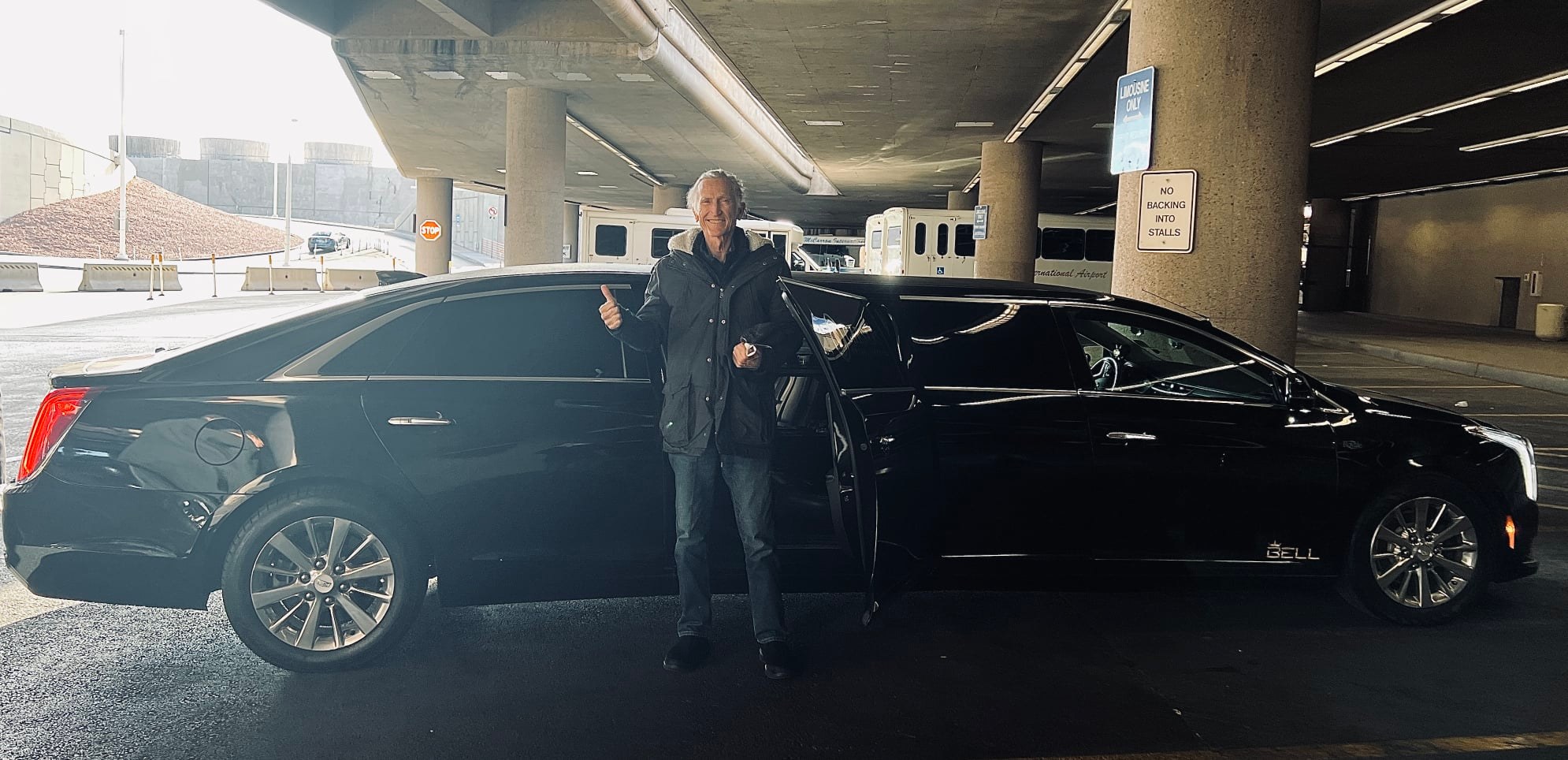 a man named patrick mithcell smiling and giving a thumbs up as he stands outside a limo at the airport