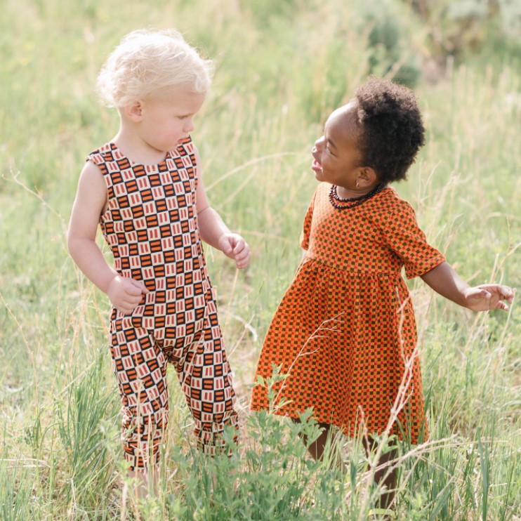 two toddlers standing and talking to each other in a field while wearing clothes from ade + ayo