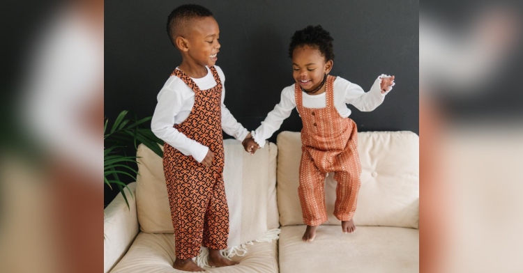 two toddlers holding hands as they jump on a couch while wearing clothes from ade + ayo