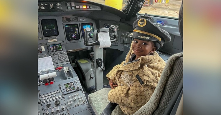 a 2 year old boy named knight james smith smiling as he wears a pilot’s hat and sits in the cockpit of an airplane