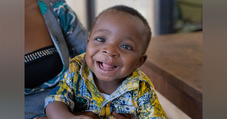 smiling baby with mom in background