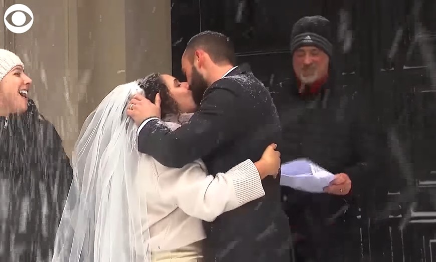 a bride named sally faulkner and a groom named adam irujo kissing outside as snow falls