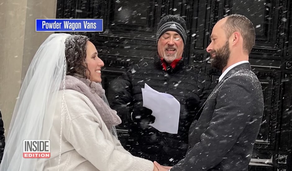 a bride named sally faulkner and a groom named adam irujo holding hands outside in the snow as adam's dad officiates their wedding