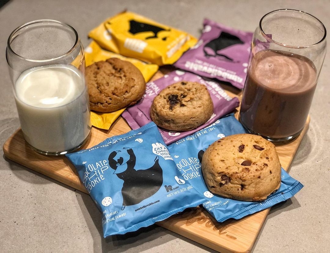 three cookies on top of bags of nunbelievable cookies that are next to a glass of milk and a glass of chocolate milk