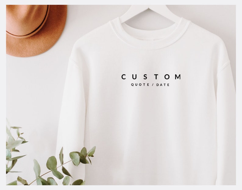 a white sweatshirt with the words "custom" and "quote / date" on it from etsy user typicallyvulgar