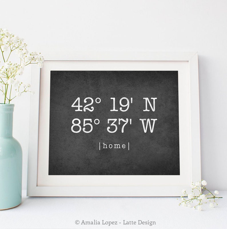 a framed print of coordinates labeled "home" that is made by etsy user lattedesign and is placed next to a vase of flowers 