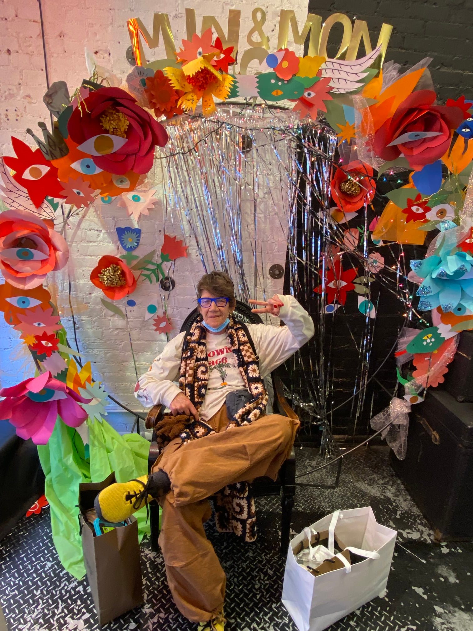 a woman named patti o'malley giving a peace sign as she sits in a chair that's surrounded by colorful decorations