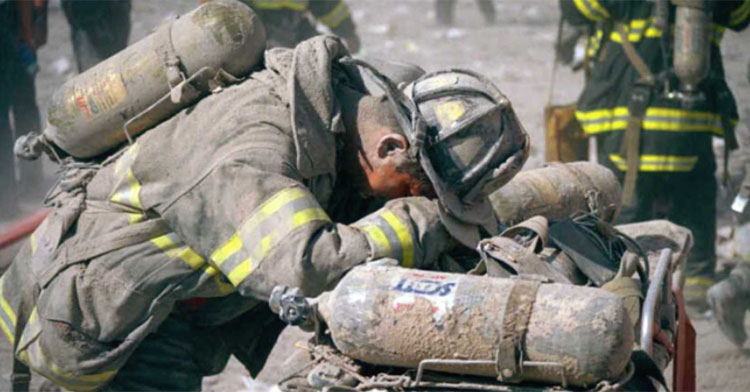 firefighter covered in ash leaning on equipment