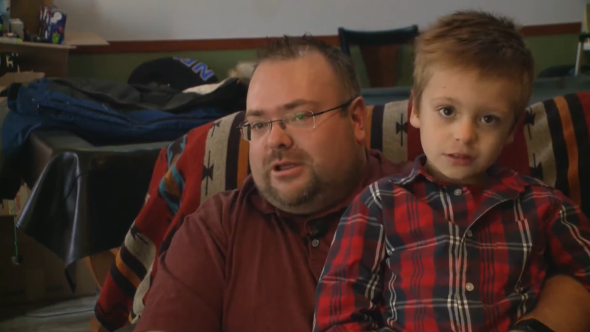 a man named brad harbert sitting on a couch and talking as his young son sits on his lap