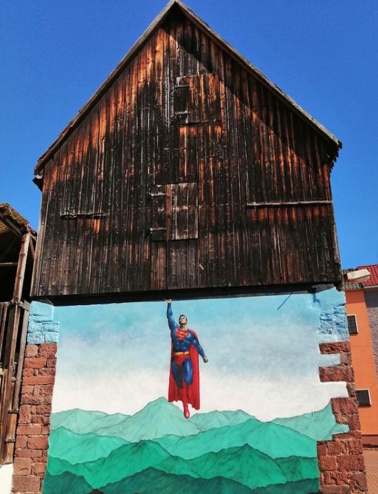 graffiti art by jps of superman flying to hold up the real building above him