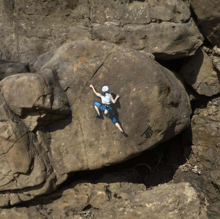 graffiti art by jps of a woman climbing that is located on large rocks