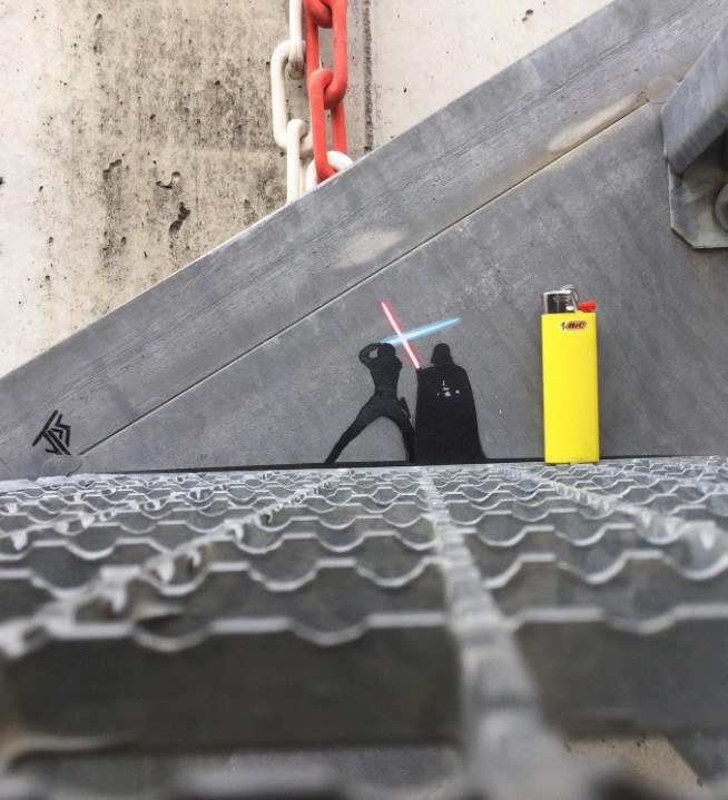 graffiti art by jps of tiny shadows of luke skywalker and darth vader fighting with light sabers next to a real lighter for size comparison 