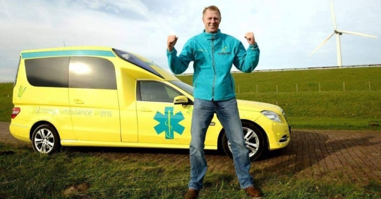 a man named kees veldboer excitedly posing in front of a yellow ambulance in the netherlands