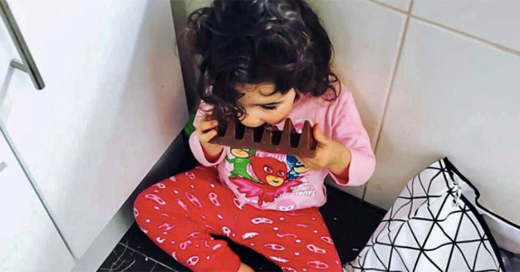 little girl in pajamas eating full bar of chocolate on kitchen floor