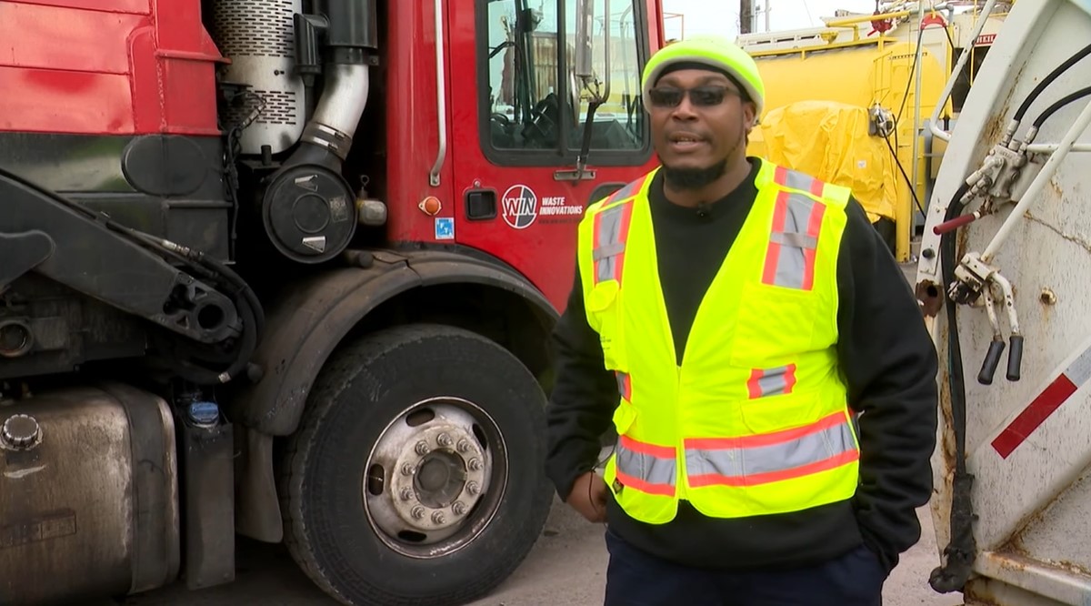 a garbage truck driver named mike nance talking to a news reporter while standing near his truck