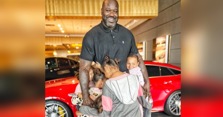 shaquille o’neal smiling wide as eight children from the collins kids on instagram hug him as they stand inside of a mercedes-benz dealership