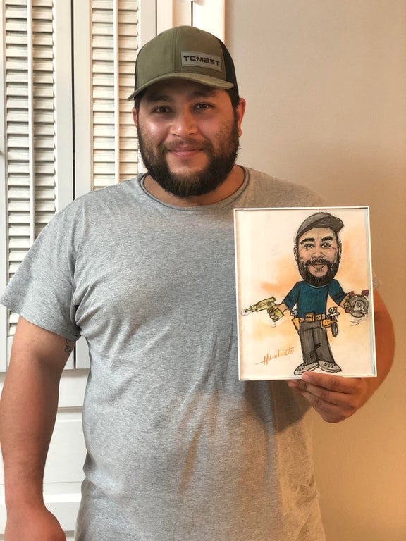 a man who works at a nursing home smiling as he shows off a drawing of himself that one of his nursing home residents drew from memory