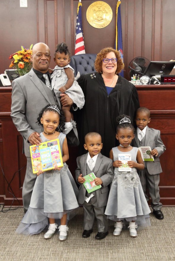 a man named lamont thomas posing with a judge and the five children he's adopting, all of which are siblings
